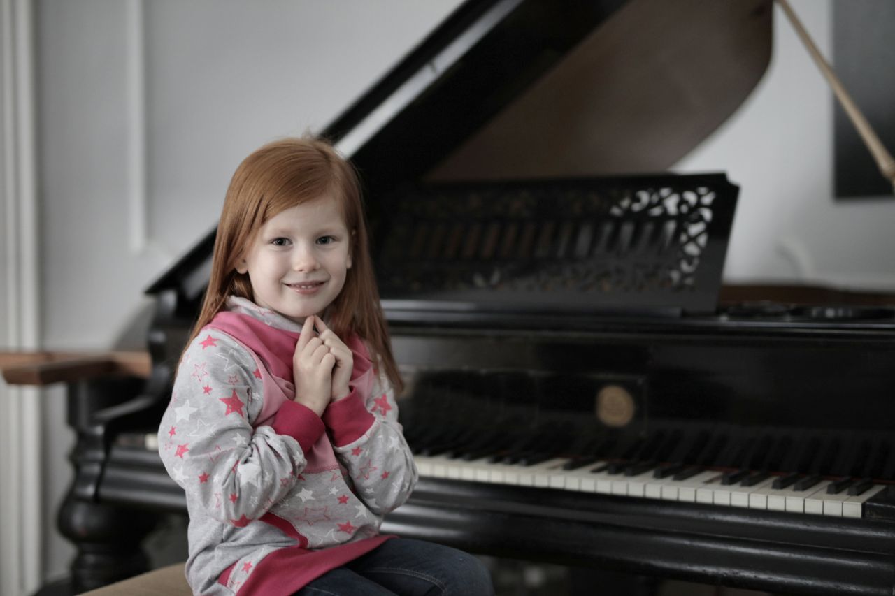 Young girl sitting by a grand piano indoors, smiling charmingly.